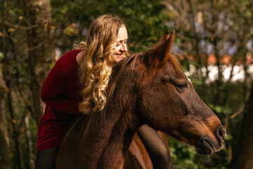 Young woman standing beside a chestnut Arab Lewitzer mix horse, showing closeness and calm connection in soft autumn light.