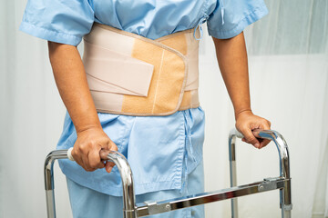 Asian senior pain back wearing elastic support belt with walker.