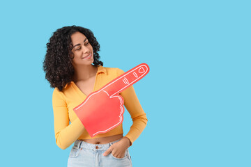 Female African-American sports fan with foam hand pointing at something on blue background