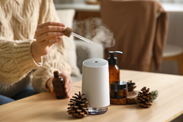 Woman with forest bumps adding essential oil to air humidifier on table in room, closeup