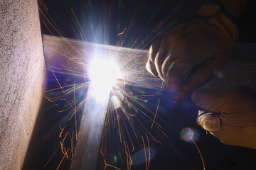 Focused welder at work, using tool for welding metal in construction industry. process creates intense heat and bright light with flying sparks, showing skilled craft