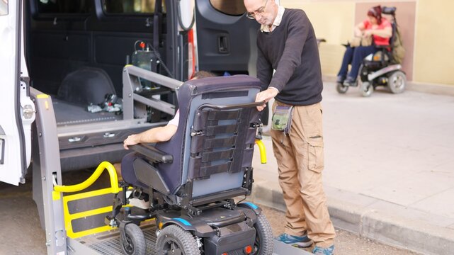 Person assisting motorized wheelchair user onto accessible vehicle lift