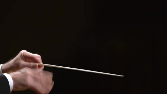 The conductor's hands, gesturing with baton, leading an orchestra in perfect harmony. The dark background adds a sense of drama and focus to the image Stock Video