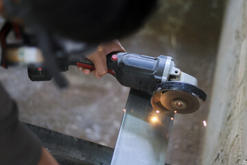 Focused worker hand grinding metal with an industrial tool. Bright sparks fly during cutting process, showing concentration and craft of labor