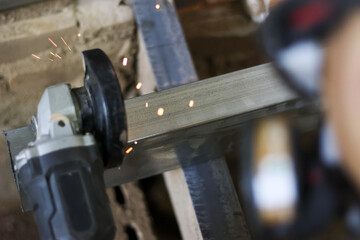 Worker with focused concentration uses hand tool for metal cutting work. This industrial angle grinder on steel bar creates bright hot spark during fabrication