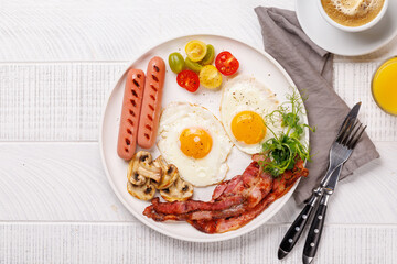 A classic breakfast plate featuring sunny-side-up eggs, crispy bacon, sausages, and fresh tomatoes