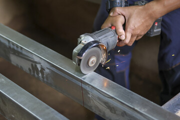 Focused worker uses an angle grinder to cut metal beam in workshop. This industrial fabrication work creates bright sparks, showing diligence, skill and precision
