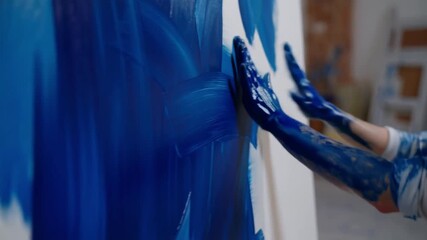 The artist passionately painting a canvas with blue color, their hands and arms covered in paint Stock Video