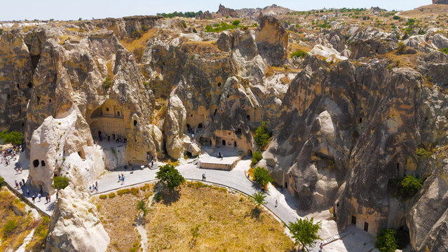 Goreme, Nevsehir, Turkey. Overhead view of Goreme Open Air Museum with tourists exploring ancient cave entrances and rock-cut churches.. Aerial View