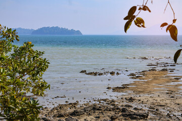 Exposed rocky tropical beach during low tide with an isolated mountainous island.