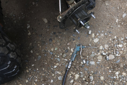 Automotive repair in progress showing vehicle hub assembly and grease gun on gravel surface. gritty, industrial focus on car maintenance and mechanic service work