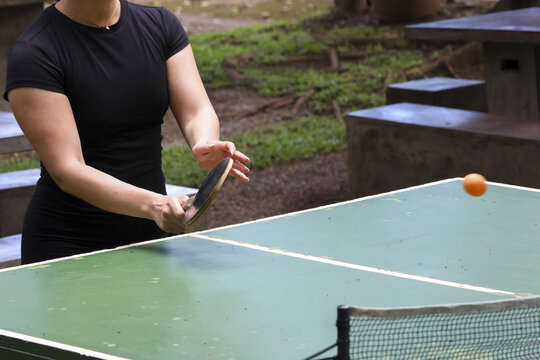 Focused woman in active play during an outdoor table tennis game. fun hobby for recreation in park, she holds her paddle ready for next shot - Powered by Adobe