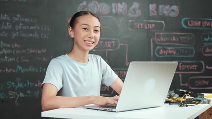 Smart girl programming system by using laptop at blackboard. high school student writing engineering code or prompt while looking at camera at STEM technology class. Creative education. Edification