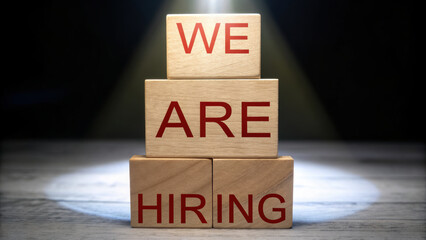 We are hiring message on wooden blocks with spotlight on dark background, symbolizing job opportunity and recruitment motivation