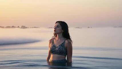 Woman in swimsuit wades through ocean waves at sunset - Powered by Adobe