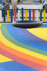 Playground swing hanging over a colorful rainbow-striped rubber safety floor, creating a cheerful atmosphere