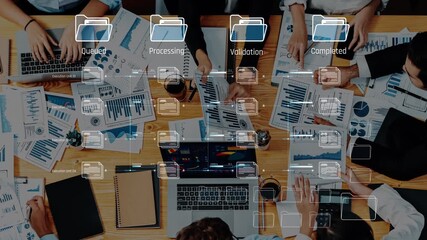 A diverse business team engaged in strategic discussions and data analysis with laptops, papers, and charts while managing project workflows in a modern office environment. Raster - Powered by Adobe