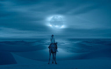 A woman riding a camel across the thin sand dunes of the in Western Sahara Desert - Beautiful sand dunes in orange desert at sunrise with crescent moon - Sahara, Morocco 
