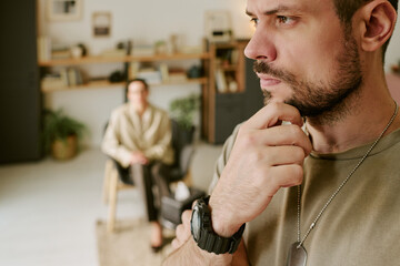 Caucasian young adult man standing in foreground touching chin appearing thoughtful, middle aged...