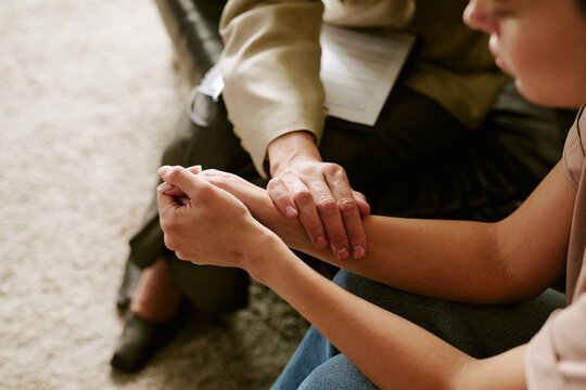 Middle aged Caucasian woman comforting young adult Caucasian woman by holding hands during therapy session, therapist supporting client in psychological counseling setting