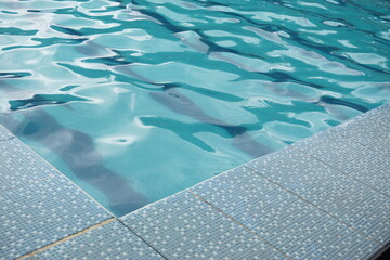 corner of a swimming pool with clear blue water, the surface of the water looks gently wavy...