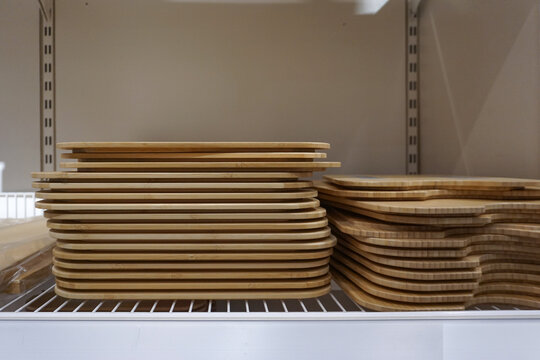Stacks of wooden cutting boards are neatly arranged in several tall, light-colored piles with a smooth and consistent grain pattern in a display case

