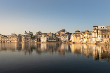 Sunrise at the sacred lakeside of holy Pushkar town in Rajasthan, with historic ghats descending to the calm water and soft morning light creating a serene spiritual atmosphere.