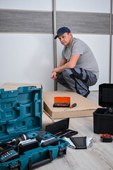 Man feeling frustrated and confused while kneeling by an unassembled furniture box and tools