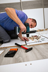 Man assembling white flat pack furniture at home with a power drill and tools