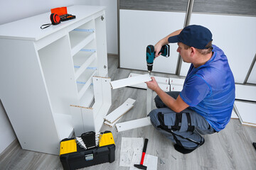Man using power tool for home improvement, assembling white cabinet in his room