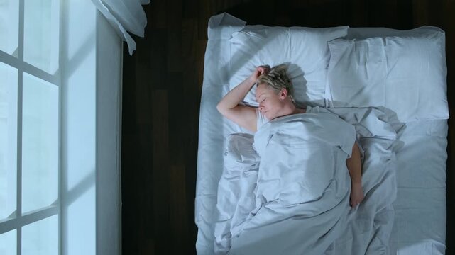 Sleeping woman tossing and turning in bed while sleep in bedroom in apartment at night, top view.