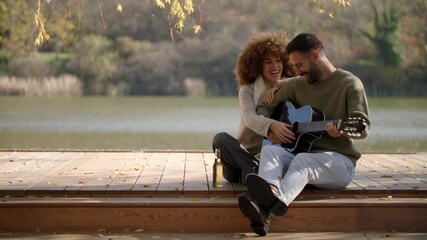 A young couple shares joyful moments by the lake, strumming a guitar and sharing smiles under the warm sun.
 - Powered by Adobe