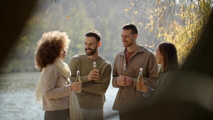 Group of friends laughs and shares drinks by the peaceful lakeside on a sunny day. Joyful moments create lasting memories together.
