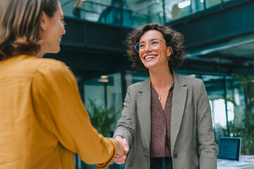 Businesswomen shaking hands with friendly smile in modern office setting.