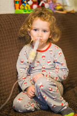 Little girl with curly hair wearing nebulizer mask for steam inhalation on brown couch. Child receiving breathing treatment at home. Pediatric healthcare for kids.