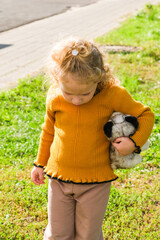 Little girl with curly hair holding a fluffy toy puppy outdoors. Child activity, innocent moment, childhood memory, happy lifestyle.