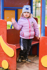 Caucasian girl child waving on a colorful playground. Happy kid playing outside. Childhood and safety concept for kindergarten background.