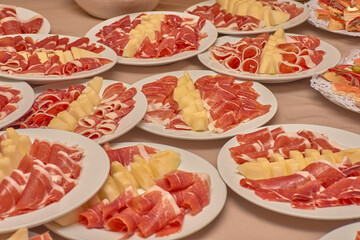 Plates of ham and melon canapes arranged in rows for serving at a large gathering with a festive and traditional atmosphere.