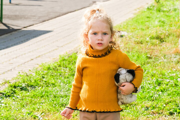 Caucasian girl with curly hair holding a stuffed animal outdoors. Child playtime and toy companionship concept for early childhood development.