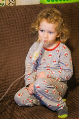 Little child with curly hair uses nebulizer at home. Small kid receiving respiratory treatment. Healthcare, asthma, allergy, virus, flue concept.