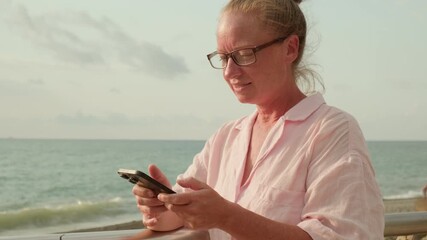 Businesswoman using smartphone while on vacation at sea while standing on embankment