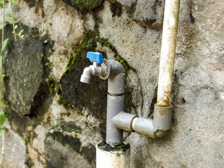 Simple outdoor water tap and plumbing system against a heavily textured, mossy rock wall. Basic household water utility detail.