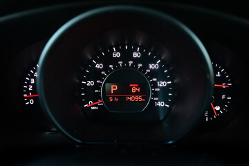 Instrument cluster of a 2017 red South Korean hatchback car showing speedometer fuel gauge and digital display through steering wheel view in daylight. Great for automotive marketing and blogs