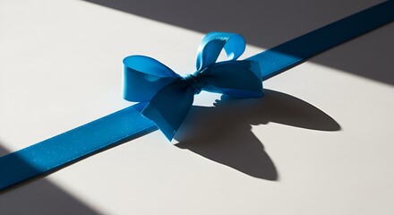 A bright blue satin ribbon bow on white surface, casting long shadows under sunlight.