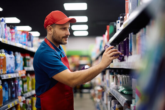 Smiling supermarket worker arranging goods on shelves at store.