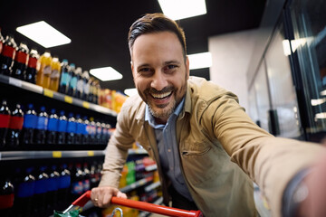 Happy man taking selfie in supermarket and looking at camera.