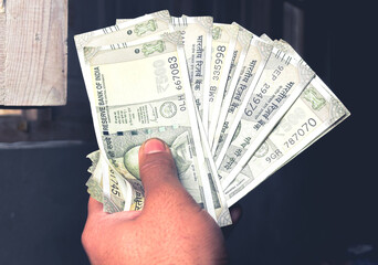 Closeup focused photo of a man showing money in his hand. A person counting cash or money in his...