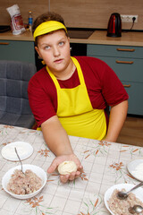 A boy in a red shirt and yellow apron is holding a dough ball