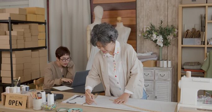 Artisan at Work: In a cozy workshop filled with spools of thread and patterns, an experienced craftswoman meticulously sketches designs, her dedication to her craft clearly evident. 