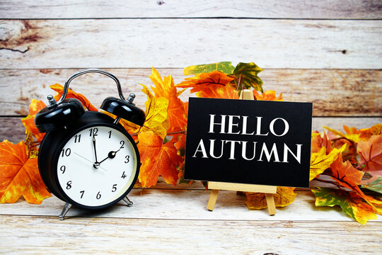 Hello Autumn text with alarm clock and maple leaf decoration on wooden background